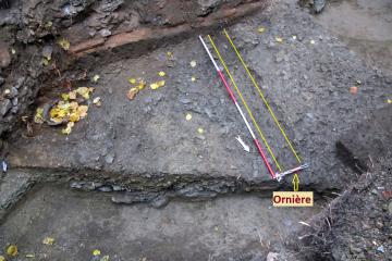 Vue partielle de la chaussée empierrée, en partie supérieure de laquelle apparaît une profonde ornière due à la circulation charretière. 