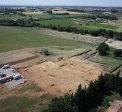 Vue aérienne du décapage sur le site néolithique final de Cadoules, dans la plaine de Mauguio. L'assombrissement des sédiments, visible au centre gauche de la photo, marque un ancien chenal de la rivière qui apparaît au second plan (rangée d'arbres). Cadoules, Mudaison (Hérault), 2013. © Archéodrone/Inrap.